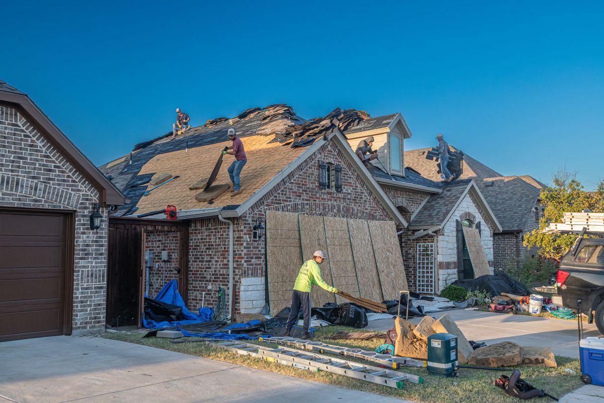 Roofers stripping an old shingle roof on a brick house before replacement